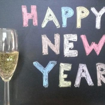champagne glass next to happy new year chalkboard sign