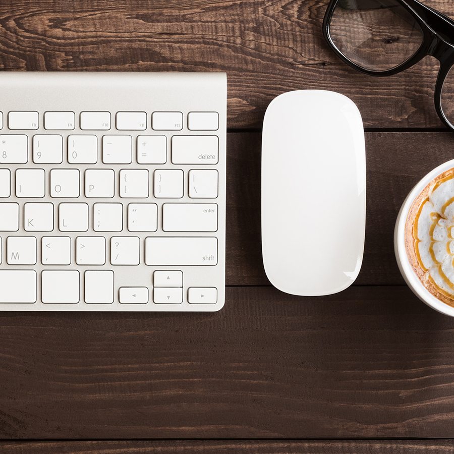 Apple mouse and keyboard on a desk next to glasses and a cup of coffee
