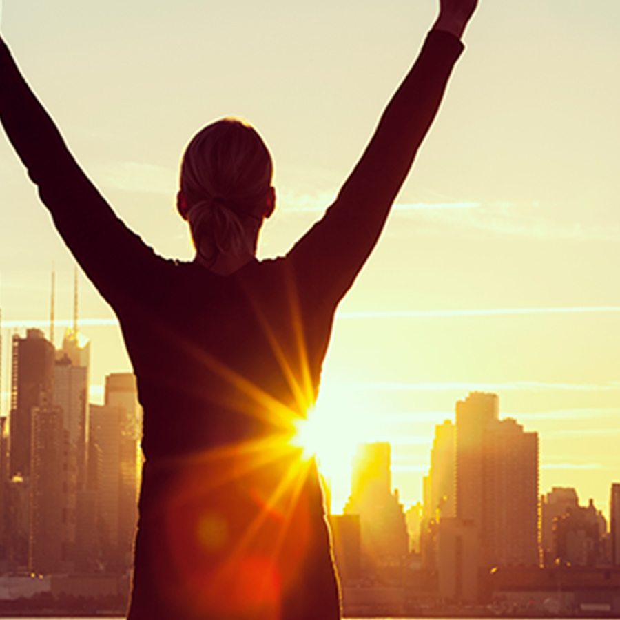 woman throwing arms up in front of sunset