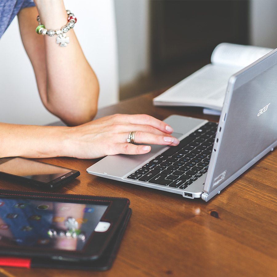 Person using laptop to work next to cell phone and iPad