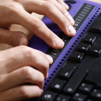 Blind person using computer with braille computer display and a computer keyboard. Blindness aid, visual impairment, independent life concept.