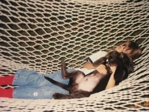 Aged photo of a young girl holding a puppy dog on hammock.