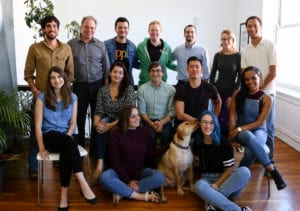 Company poses while dog licks woman's ear.