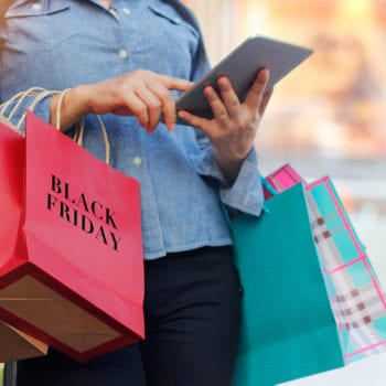 Woman using tablet and holding Black Friday shopping bag while standing on the stairs with the mall background