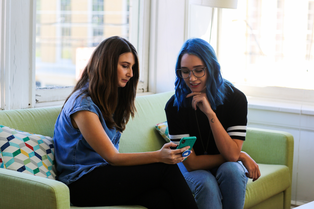 Two female Optimists sitting on couch and looking at phone