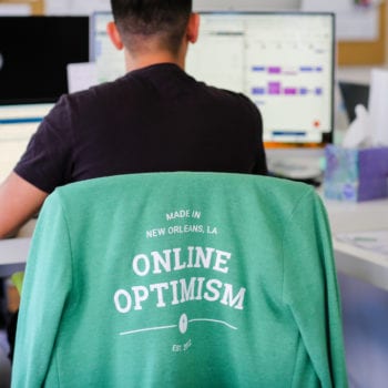 Optimist working at desk with Optimist shirt on chair