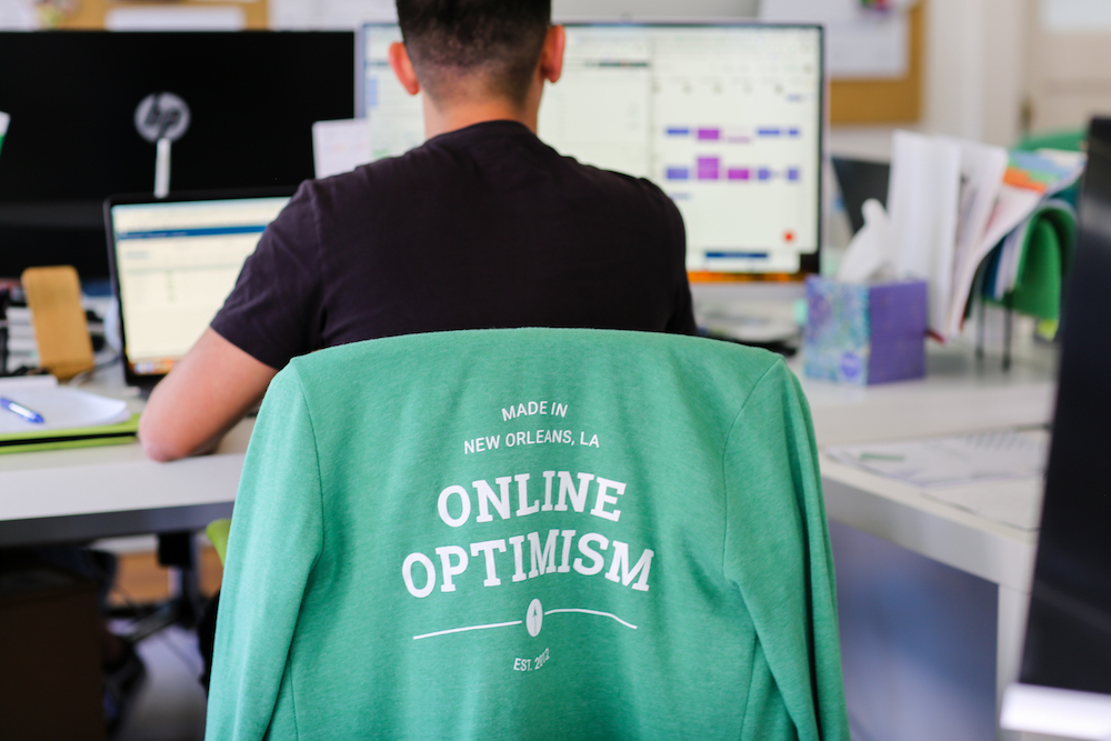 Optimist working at desk with Optimist shirt on chair