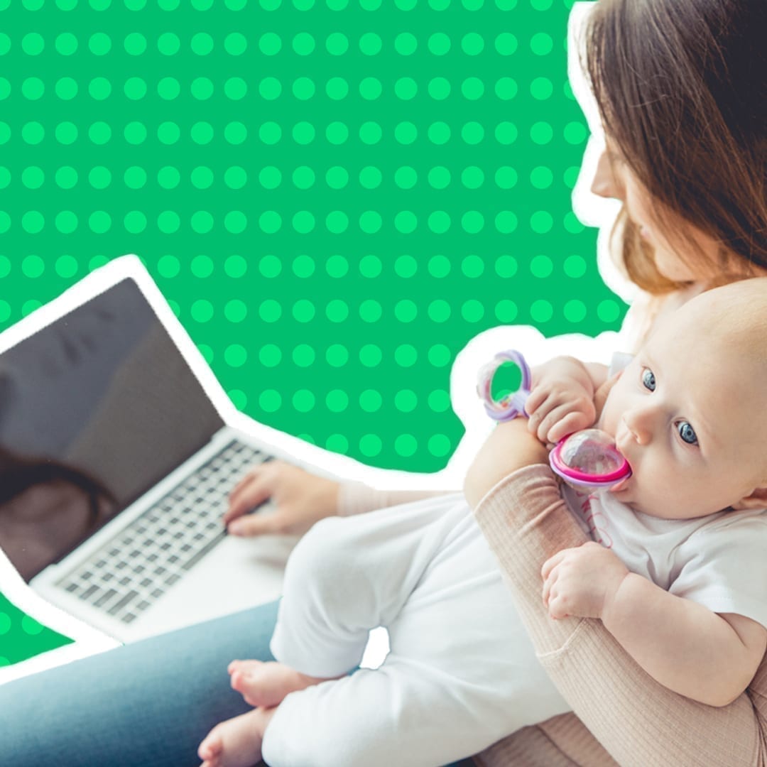 A woman holds her baby as she works on a laptop