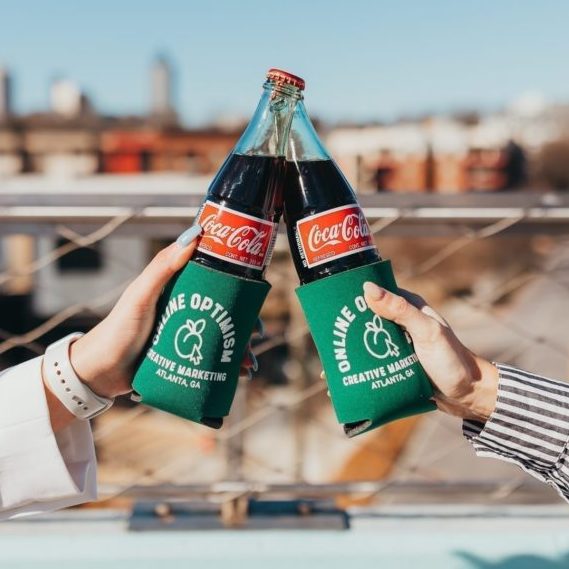 Optimists cheers with glass bottles of Cokes in Online Optimism drink holders