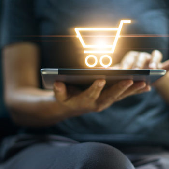 Person holding tablet with a glowing shopping cart icon