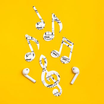 Wireless headphones and music notes cut from paper on a yellow background. Music imitation concept. Copy space