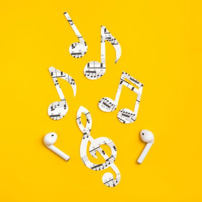 Wireless headphones and music notes cut from paper on a yellow background. Music imitation concept. Copy space
