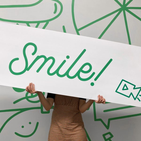 Optimist holding a branded sign reading "Smile!"