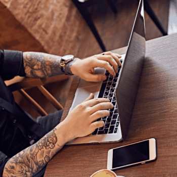 Tattooed hands typing at a computer