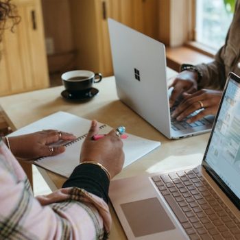 Two entrepreneurs on laptops at a table asking each other, "Is it too late to start blogging?"