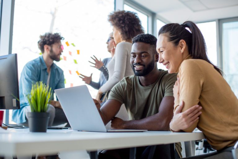 A team working on a design project. Two people work at a computer while three people discuss ideas.