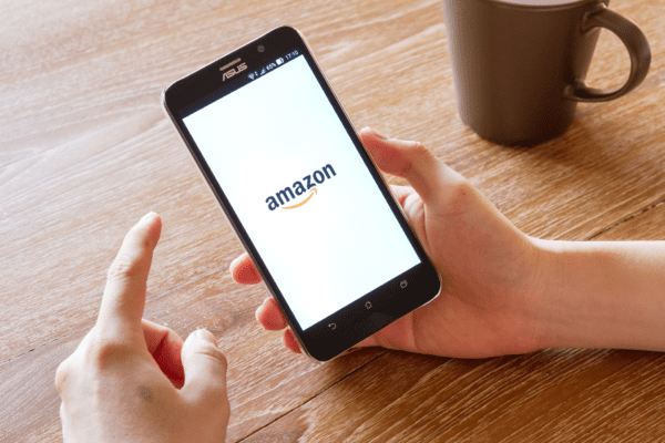 Hands hold a cellphone with the Amazon shopping logo pulled up onscreen