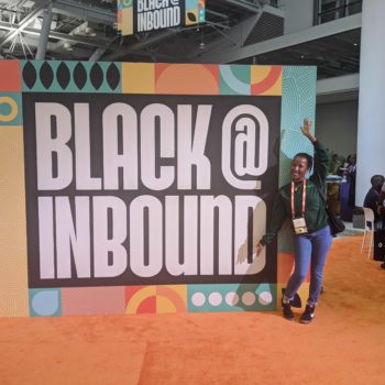 Our Business Development Director, Irene Muchai at the Hubspot Inbound Conference, standing next to a sign that reads "Black @ Inbound"