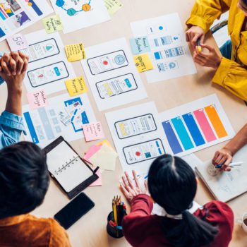 group of people sitting around a table with design mockups