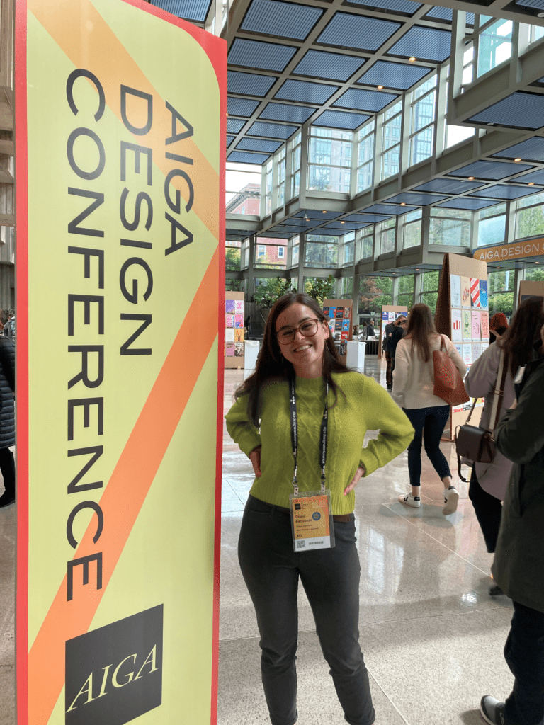 Claire stands next to an AIGA Design Conference sign at the Seattle Convention Center