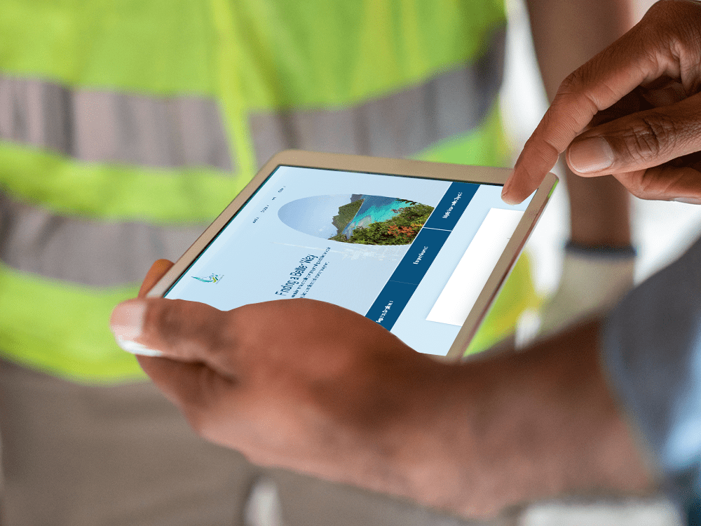 A person on a construction site holds a white tablet, looking at L&M Environmental Response’s website. Another person in a yellow high-visibility vest stands in the background.