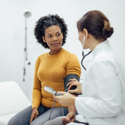 woman sitting with doctor as she administers a blood pressure check