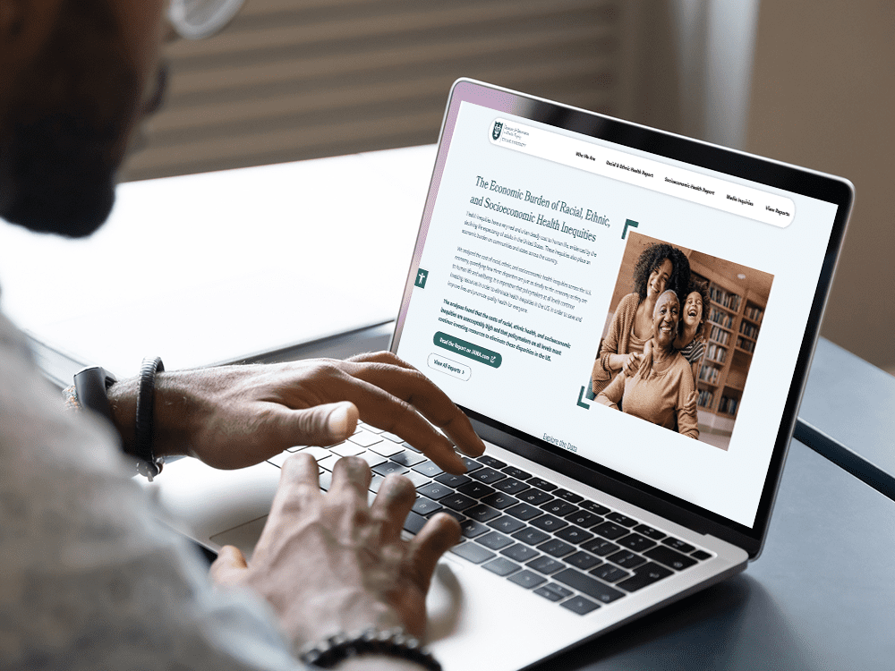 A person wearing glasses views the Cost of Inequity website on a laptop, sitting at a desk next to a window.