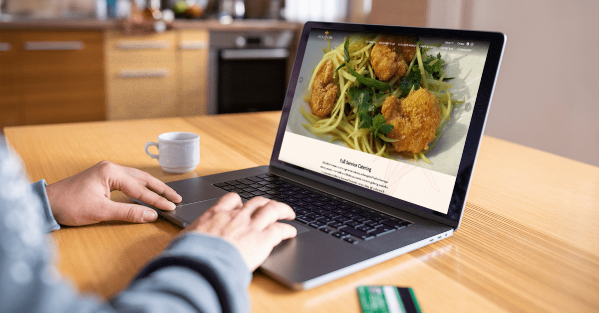 A person browses the Nolavore website on a laptop at their kitchen table.